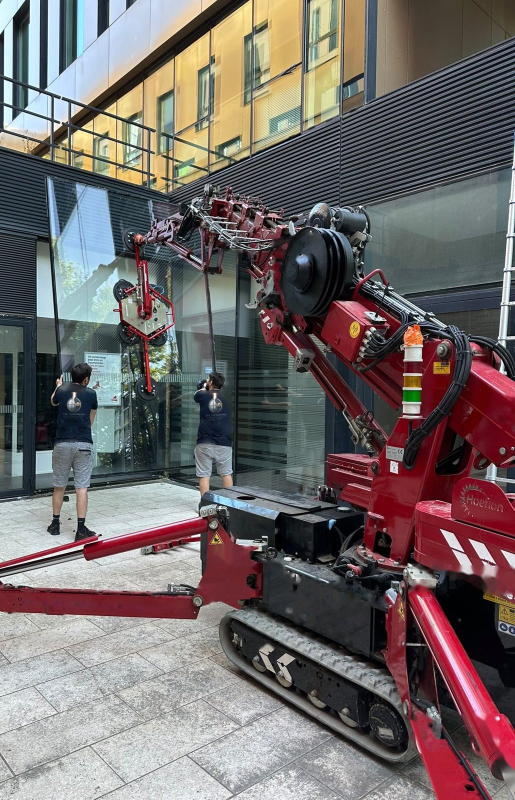 Deux vitriers des Alchimistes du Bâtiment posent un vitrage de grande dimension au robot de levage